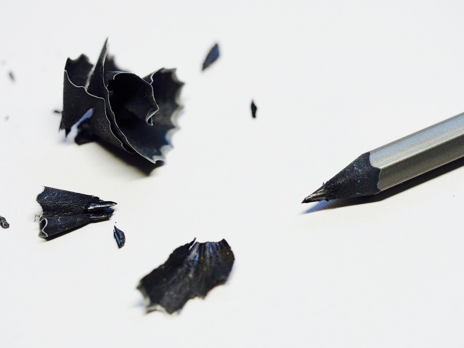 Black and white image of a sharpened pencil with pencil shavings nearby.